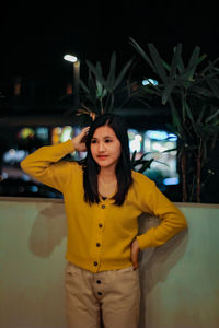 Portrait of beautiful young woman standing against yellow indoors