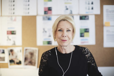 Portrait of smiling senior businesswoman with headphones against bulletin board at creative office