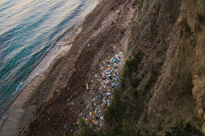 High angle view of garbage by cliff at beach during sunset