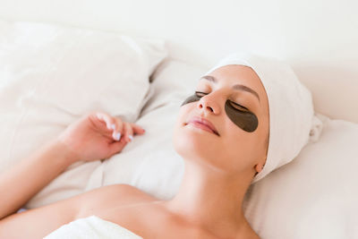 High angle view of young woman with patches under eyes lying on bed at home