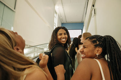 Portrait of happy teenage girl standing by female friends laughing in mall