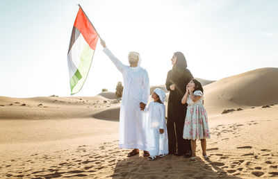 Arabian family holding flag while standing at desert against sky