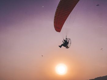 Low angle view of person paragliding against sky during sunset