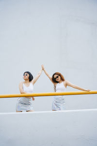 Young woman with arms raised standing against wall