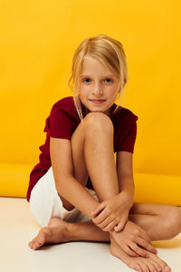 Young woman sitting against yellow background