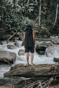 Rear view of man standing by waterfall in forest