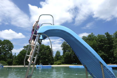 Side view of girl climbing steps of water slide in resort against cloudy sky