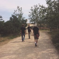 Boys with skateboard walking on footpath against sky