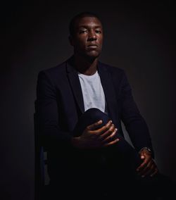 Portrait of serious man sitting on chair against black background