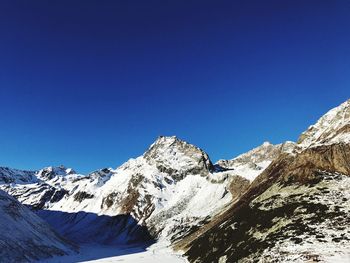 Low angle view of snowcapped mountains against clear blue sky