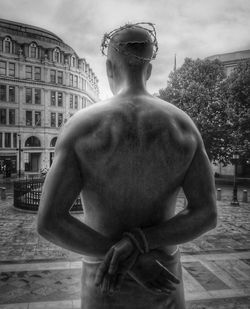 Rear view of shirtless man standing against statue in city