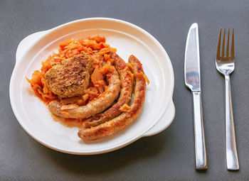 Stewed cabbage with fried sausages and a frikadelle on white plate on gray background.