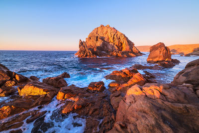 Rock formations on shore against clear sky