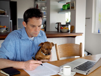 Businessman with dog doing paperwork at desk in home