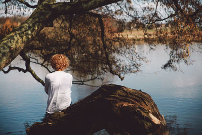 Rear view of woman sitting on fallen tree in front of lake