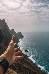 Cropped hand of man gesturing against sea