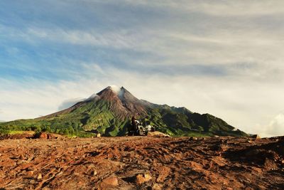 Off-road vehicle on mountain against cloudy sky during sunny day