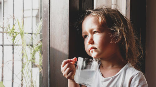 Close-up of girl holding drink looking through window