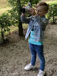 Full length of boy holding camera while standing on land