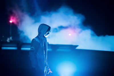 Man standing against illuminated light trails at night