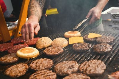 Midsection of man preparing burgers on barbecue grill