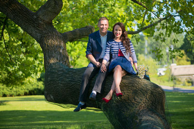 Portrait of man and woman sitting on tree trunk at park