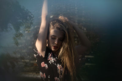 Close-up of young woman with hand raised standing against plants