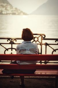 Rear view of woman sitting on bench against lake