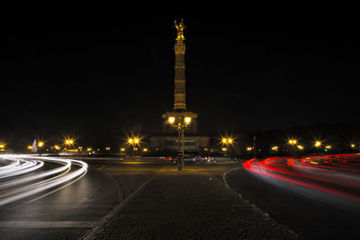 Statue by light trails on road at night