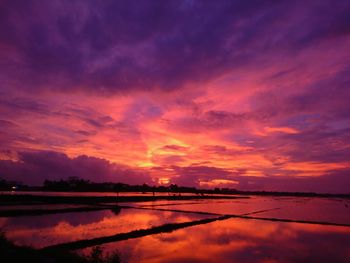 Scenic view of lake against dramatic sky during sunset