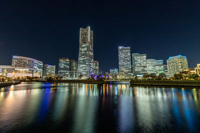 Illuminated buildings by river against sky at night