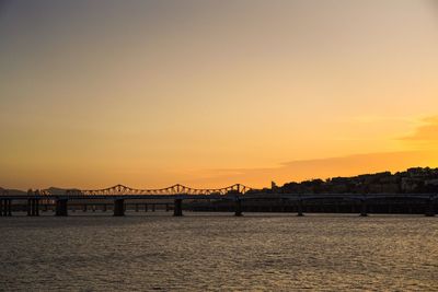 Silhouette bridge over calm river against sky during sunset