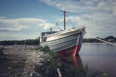 Abandoned boat moored at shore against sky