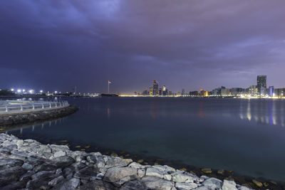 Illuminated buildings by river against sky at night
