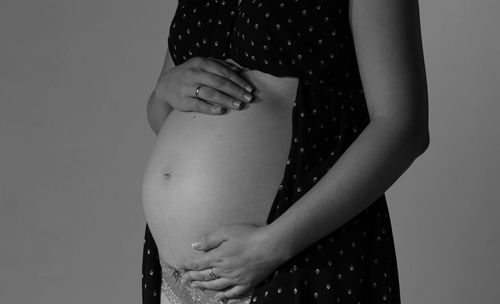 Midsection of pregnant woman touching abdomen against wall