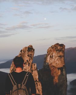 Rear view of backpacker looking at mountains against sky during sunset