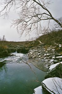 Stream flowing by lake against sky during winter