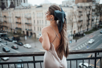 Rear view of young woman standing against railing in city