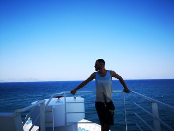 Man standing in boat against clear blue sky