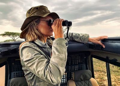 Woman sitting on car against sky