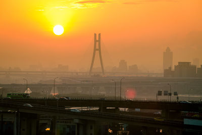 Bridge over river in city against orange sky