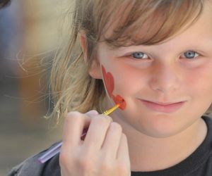 Close-up portrait of cute smiling girl painting heart shapes on cheek