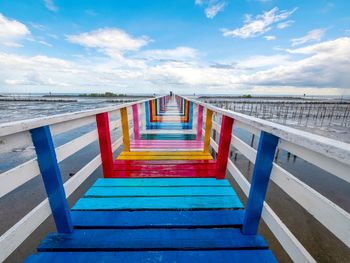 Empty boardwalk by sea against blue sky