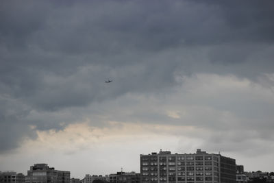 Low angle view of airplane flying over city against sky