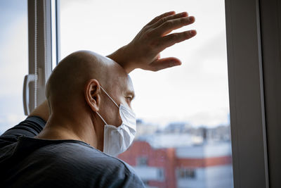 Portrait of a man in a protective mask looks through the windows to the street