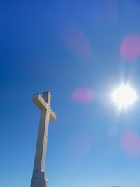 Low angle view of cross against blue sky on sunny day