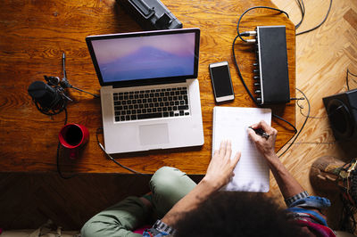 Male afro musician writing notes by laptop on table at home