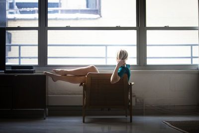 Side view of woman with hand in hair sitting on armchair at home