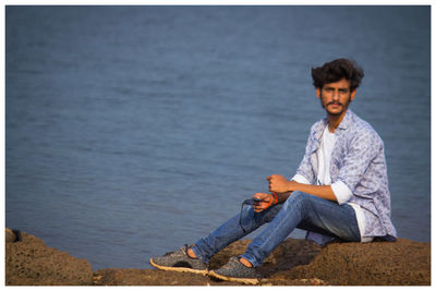 Portrait of young man sitting on rock at lakeshore