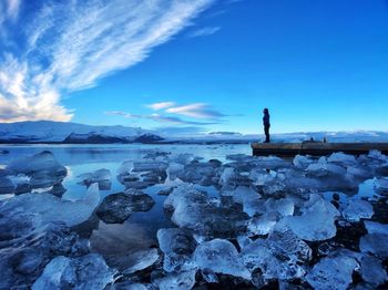 Woman standing on pier by lake covered with ice against sky